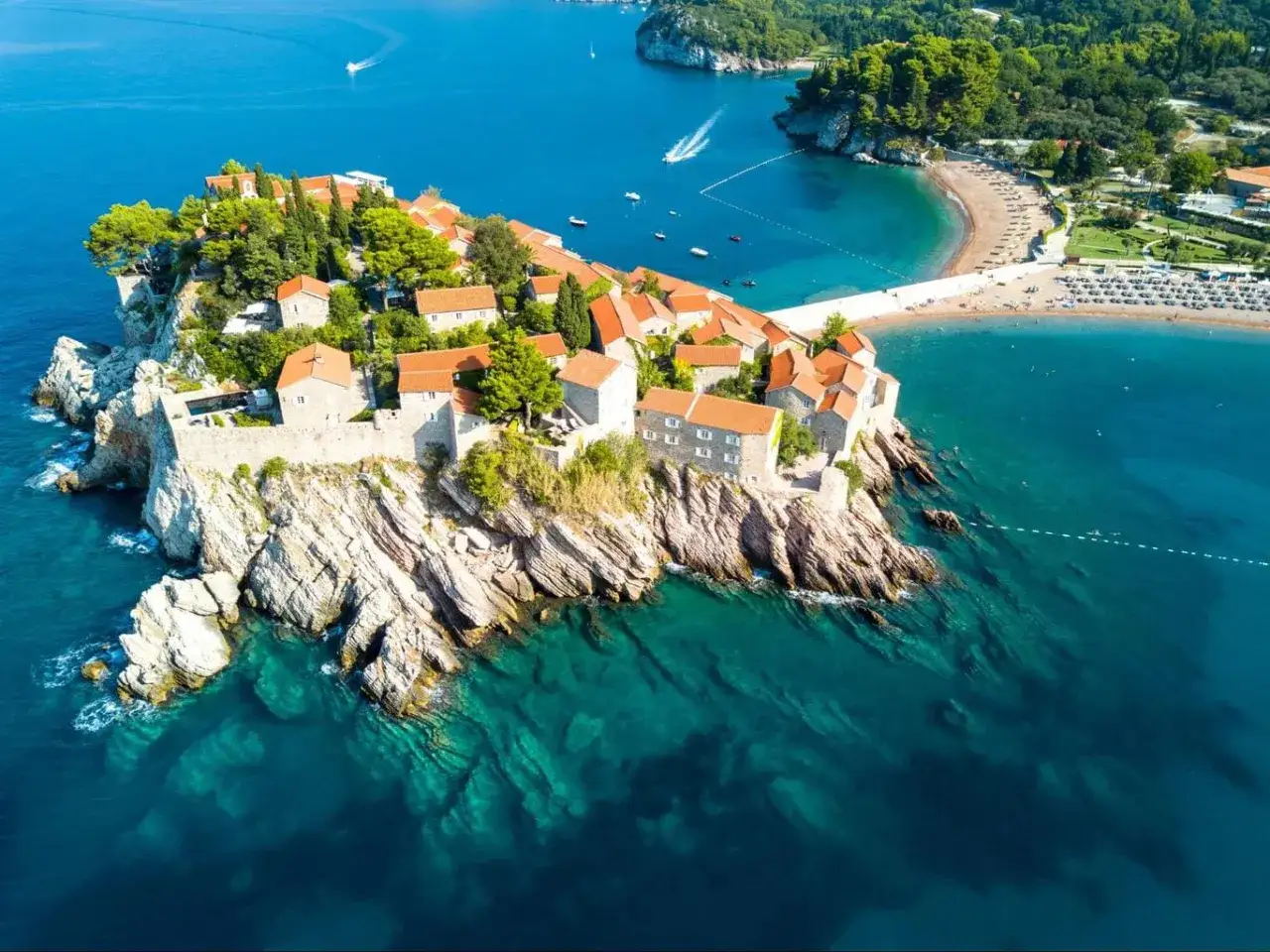 Malownicza wyspa z kamiennymi domami i czerwonymi dachami, połączona z lądem groblą, przy kt&oacute;rej rozciągają się piaszczyste plaże. Zatoka Kotorska zachwyca turkusową wodą.