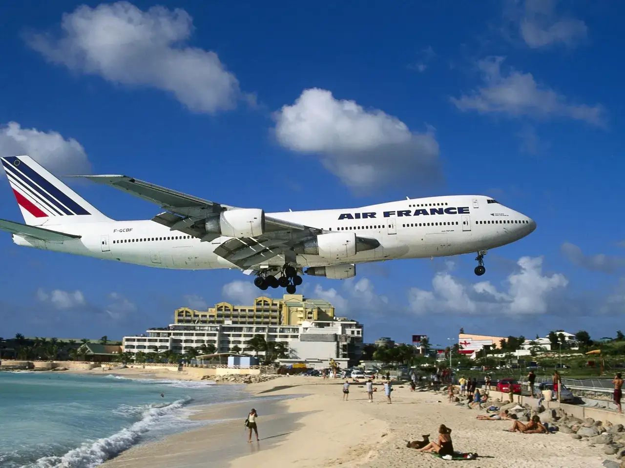 Samolot Air France nisko nad plażą, tuż przed lądowaniem. W tle hotele i turkusowe morze. To wyjątkowe lotnisko przy plaży.