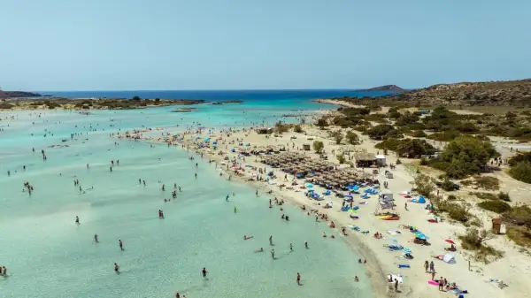 Piękna, słoneczna kreta pogoda w lipcu. Tłumy ludzi kąpią się w krystalicznie czystej wodzie i odpoczywają na piaszczystej plaży pod parasolami.
