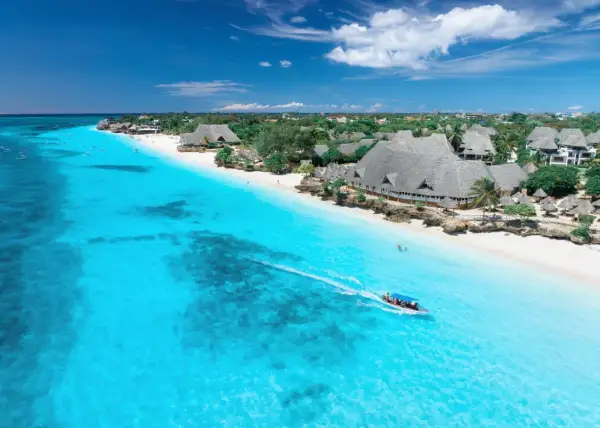 Idealna pogoda na Zanzibarze w październiku: turkusowa woda, biała plaża i łódź z turystami.