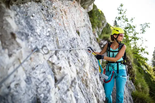 Kobieta w kasku i sprzęcie wspinaczkowym pokonuje via ferrata, czyli ubezpieczoną trasę w górach.