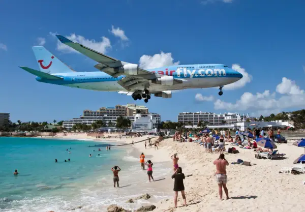 Samolot Airfly.com nisko przelatuje nad plażą pełną turystów. To słynne lotnisko przy plaży, gdzie można poczuć podmuchy odrzutowców.