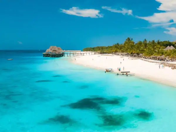 Zanzibar w lutym: słoneczna plaża, turkusowa woda, palmy i drewniany pomost. Idealna pogoda na wakacje.
