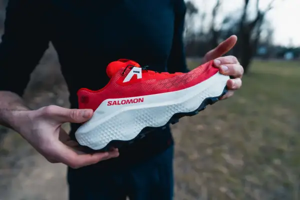 Czerwony but Salomon Ultra Glide 4 w rękach biegacza, gotowy na trailowe przygody.