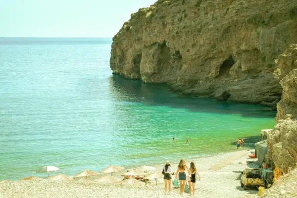 Kreta, sierpień: trzy dziewczyny idą na plażę z turkusową wodą i skalistymi klifami. Idealna pogoda na wakacje.