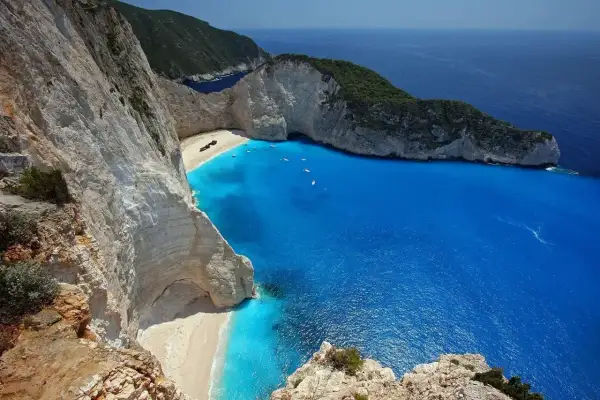 Widok na Zatokę Wraku na Zakynthos, Grecja. Wrak statku leży na piaszczystej plaży otoczonej białymi klifami i turkusowym morzem.