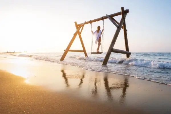 Dziewczyna na huśtawce na plaży w Turcji, fale obmywają piasek, złote światło zachodu słońca.